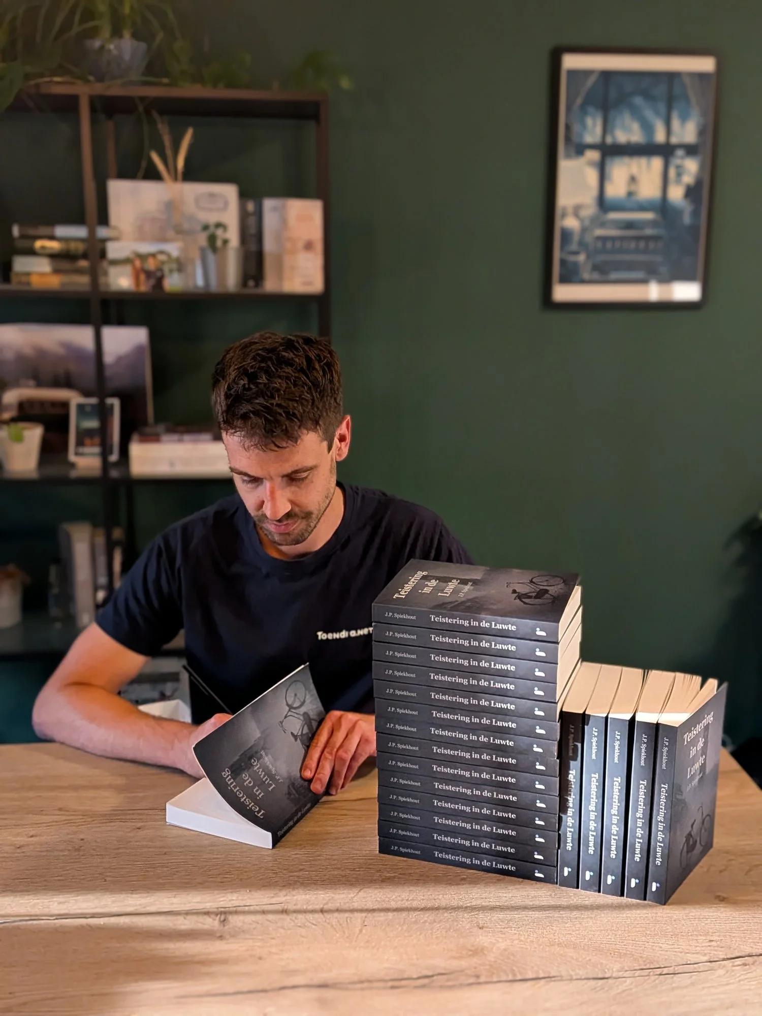 Jorim signeert een exemplaar van Teistering in de Luwte naast een stapel boeken